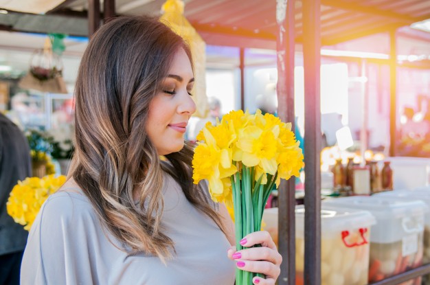 mujer sonriente joven que selecciona las flores frescas close up retrato de perfil de una bella y joven mujer disfrutando y oler un ramo de flores mientras esta de pie en un puesto fresco mercado floral durante un dia soleado al aire libre 